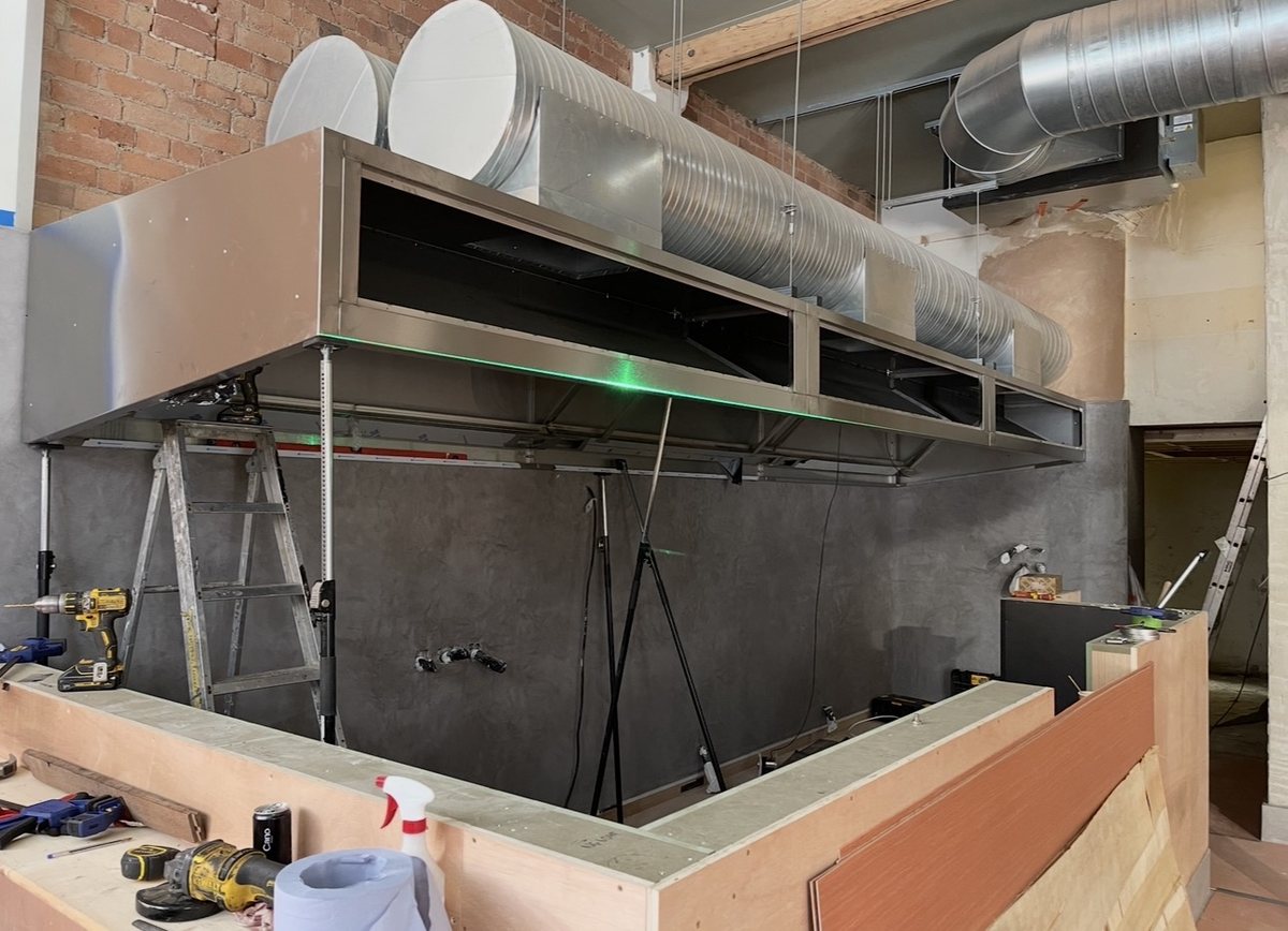 Bespoke stainless steel extraction canopy installed over a bar servery in an exposed-brick venue by Castle Catering Engineers